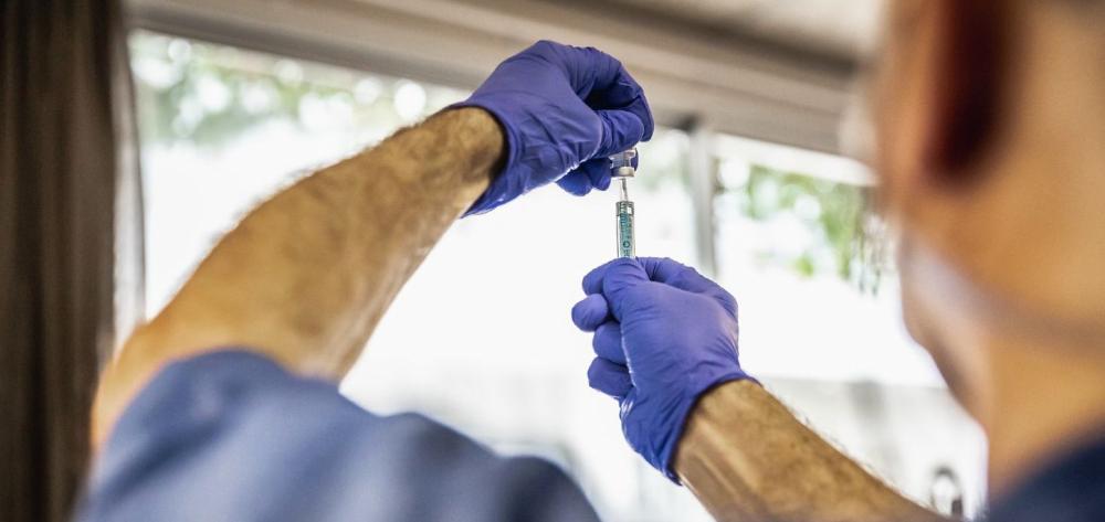 Male nurse with his back turned, emptying a vial into a syringe.