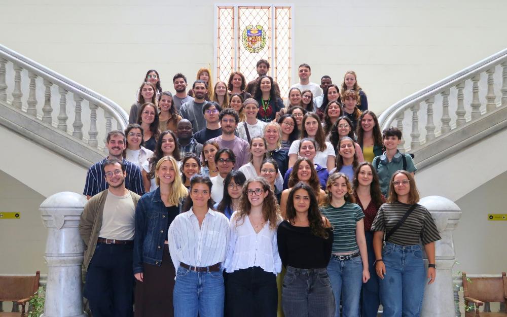 Group photo of those attending the PhD Symposium posing on the grand indoor staircase at the Faculty of Medicine and Health Sciences of the University of Barcelona (UB).