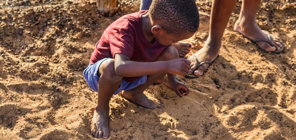 Nen africà descalç sobre el sòl de sorra i tocant-la amb les mans