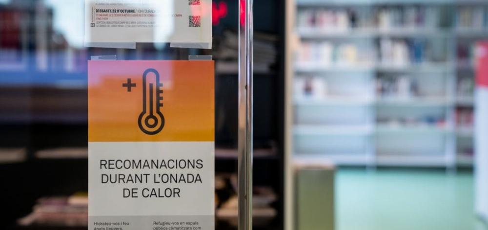 Cartell a la porta d'entrada d'una biblioteca de Barcelona amb recomanacions durant l'onada de calor amb la imatge d'un termòmetre de colors càlids