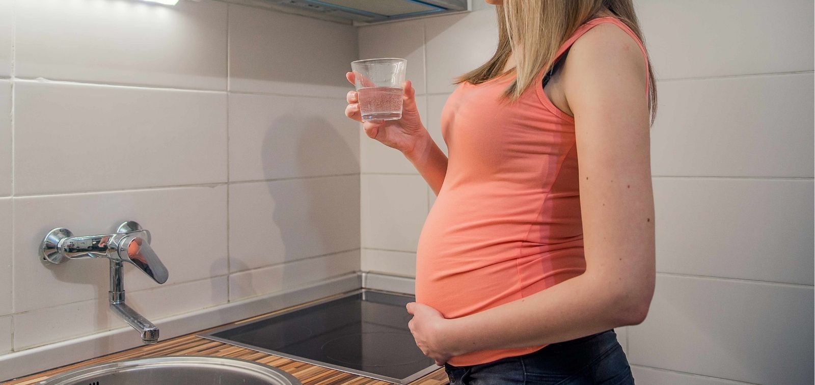 Mujer embarazada en verano con calor y un vaso de agua en la cocina