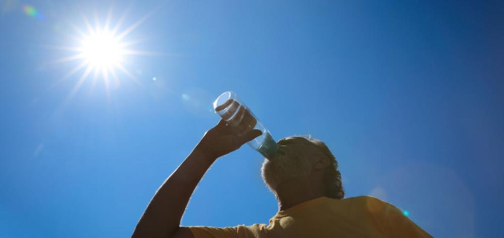 A person hydrating on a hot day with the sun in the background