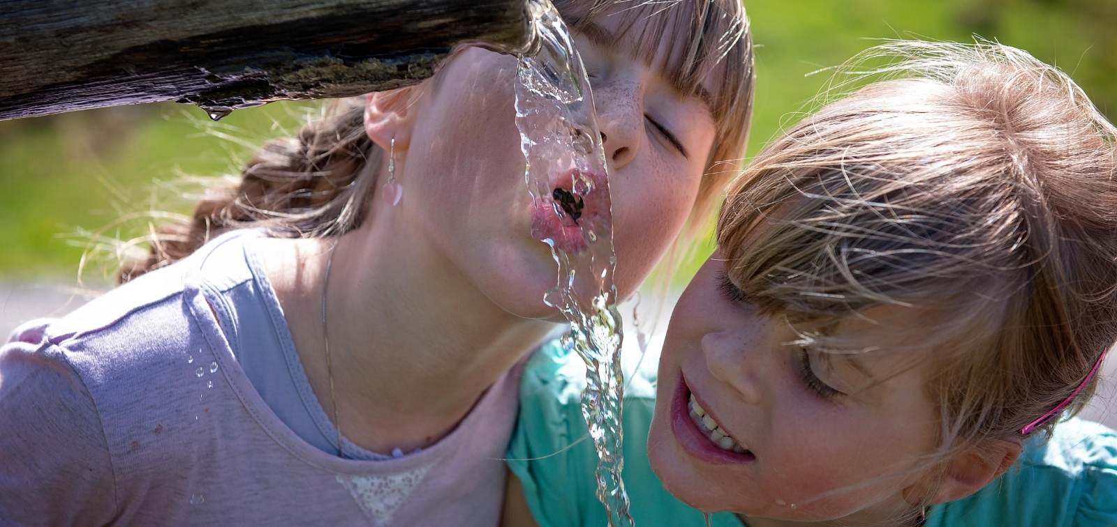 Dos niñas beben agua de una fuente