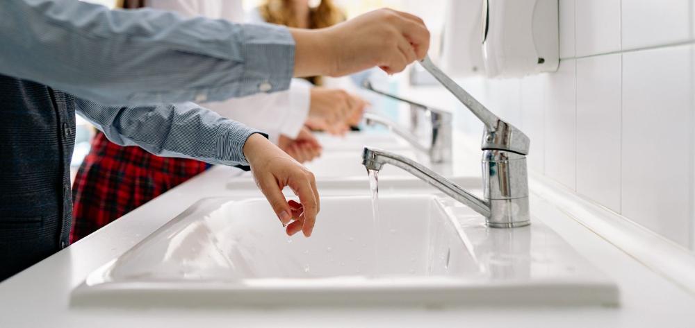 Manos abriendo el grifo de un baño y chorro de agua saliendo.
