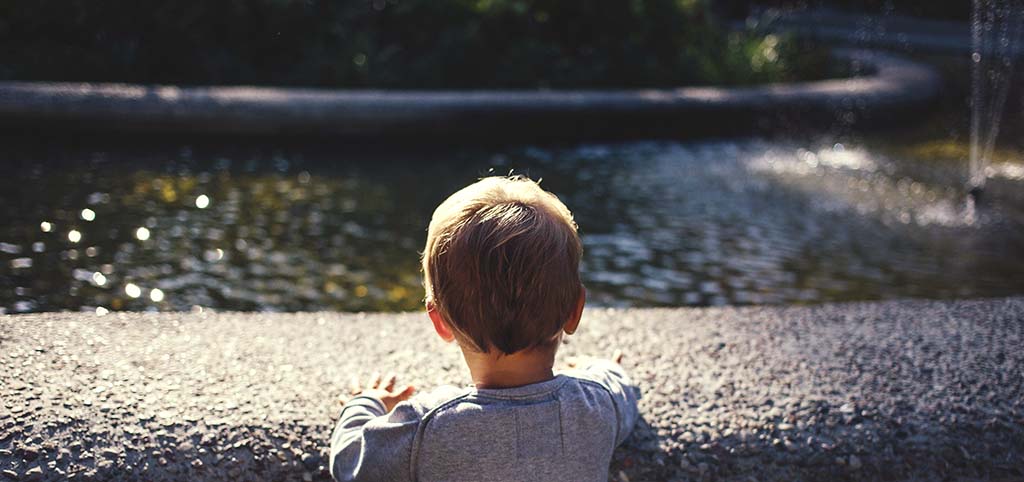 Un niño, de espaldas, juega con el agua de la fuente de un parque