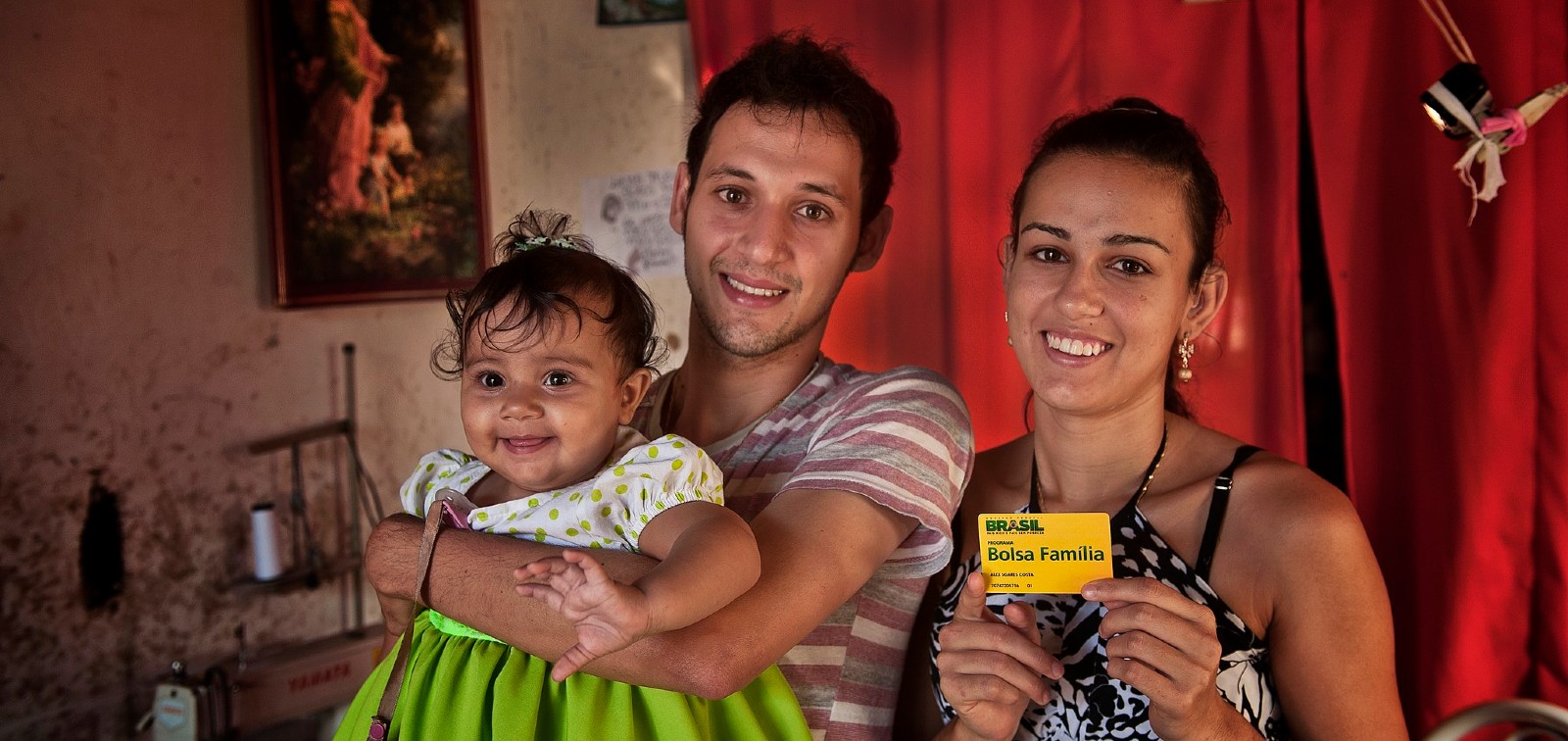 Família beneficiária apresenta o cartão do Bolsa Família em casa